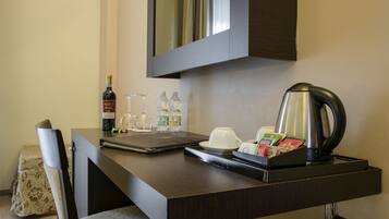 Escritorio de habitación de hotel con una computadora portátil, una botella de vino, copas, cafetera y bolsitas de té.