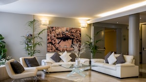 A modern living room with a glass coffee table, white sofas, and decorative plants. - Hotel Executive (Siena)