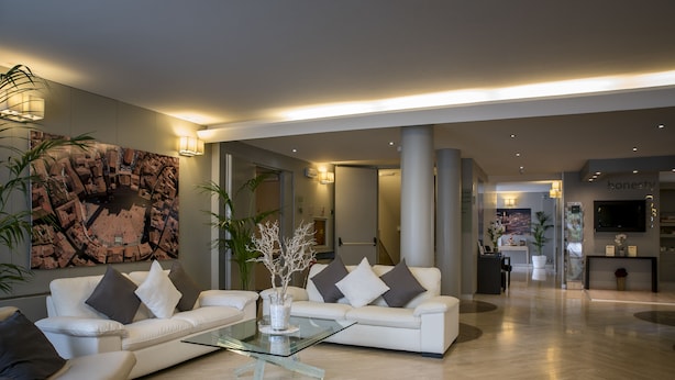 A spacious lobby with a modern white sofa set, a glass coffee table, and a large abstract painting on the wall. - Hotel Executive (Siena)