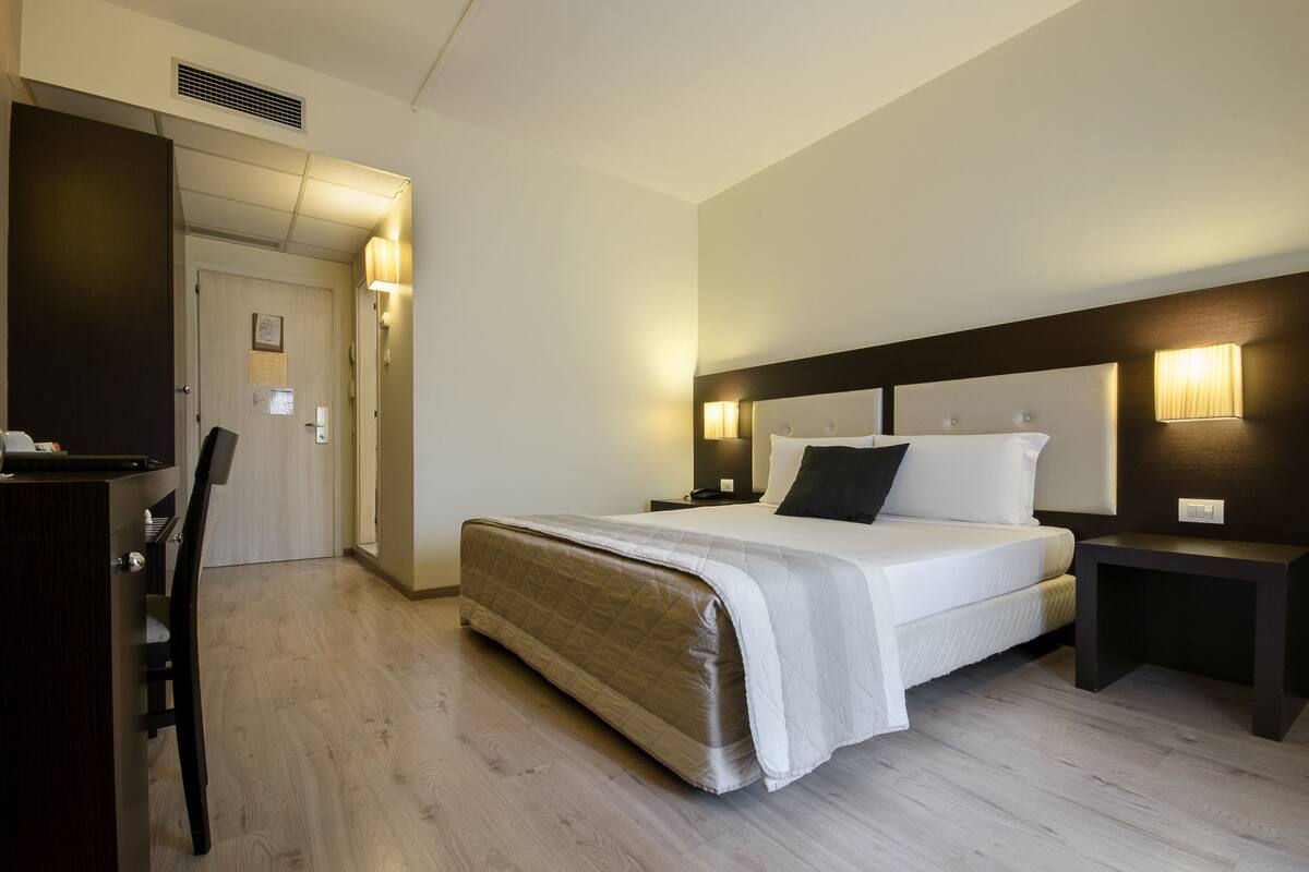 Una habitación de hotel con una cama, mesitas de noche, un escritorio y una silla.