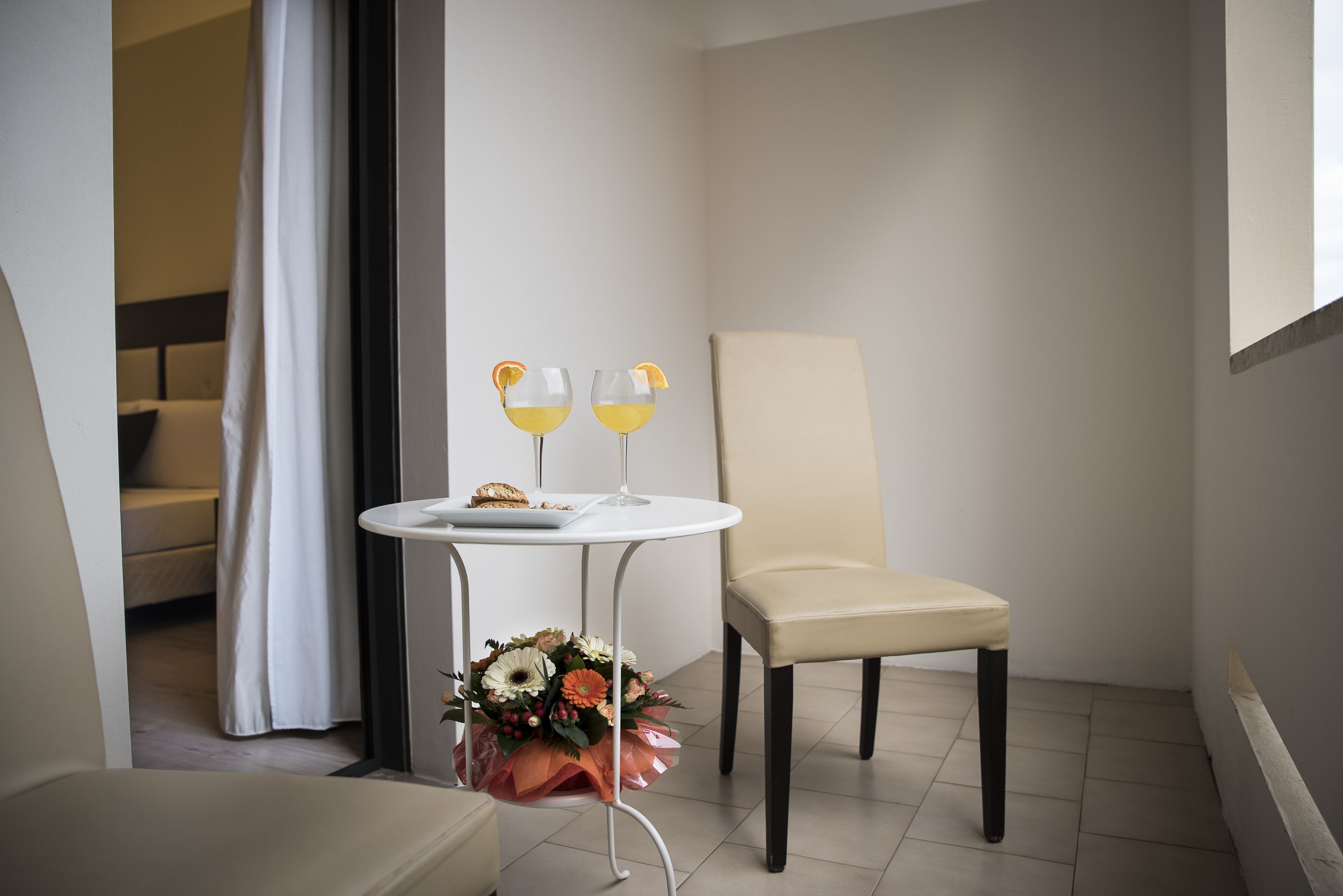 A small, modern room with a round table, two chairs, a bouquet of flowers, and two glasses of a yellow beverage.