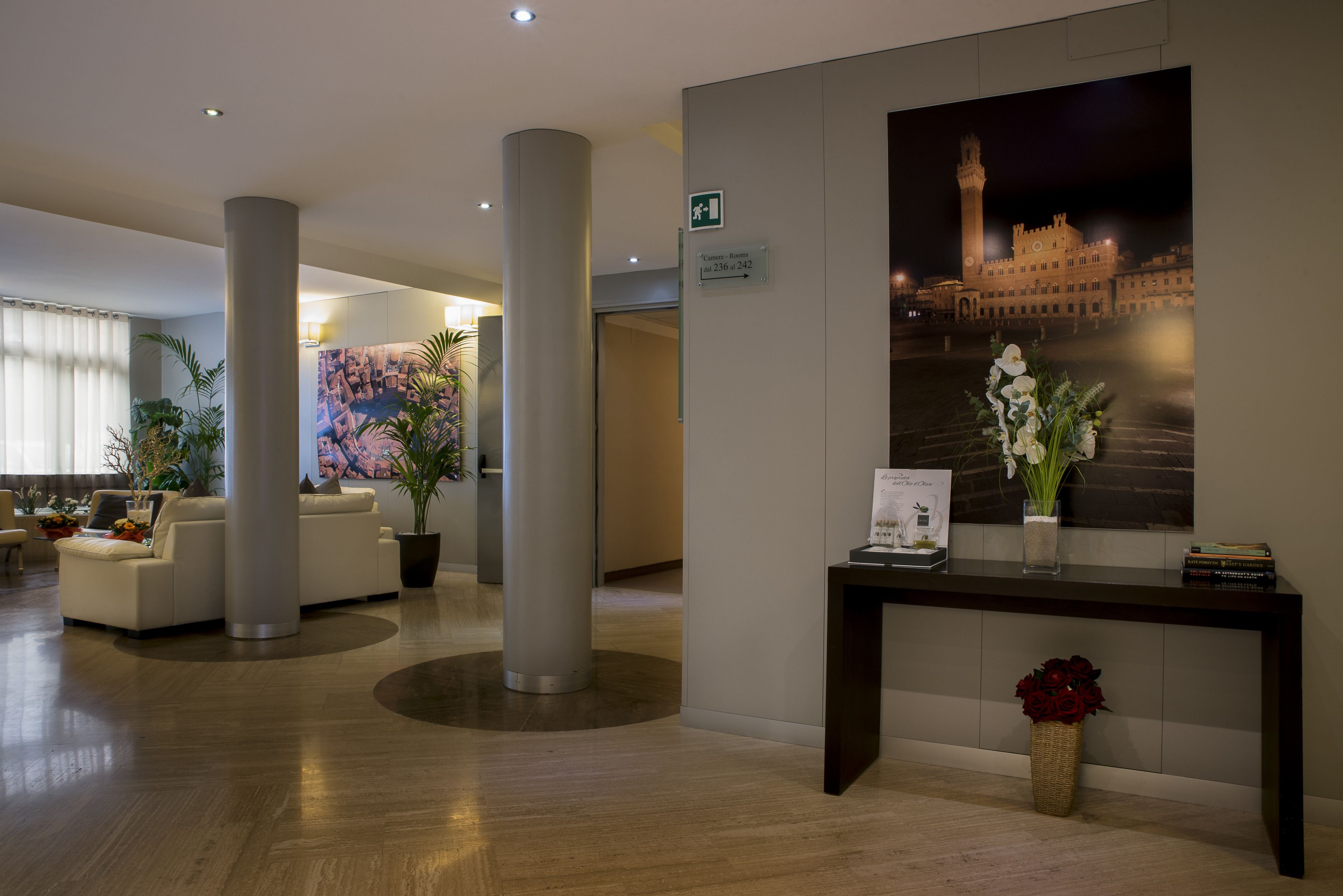 A lobby with a reception desk, a large pillar, a sofa, and a wall-mounted sign indicating the location of the lobby.