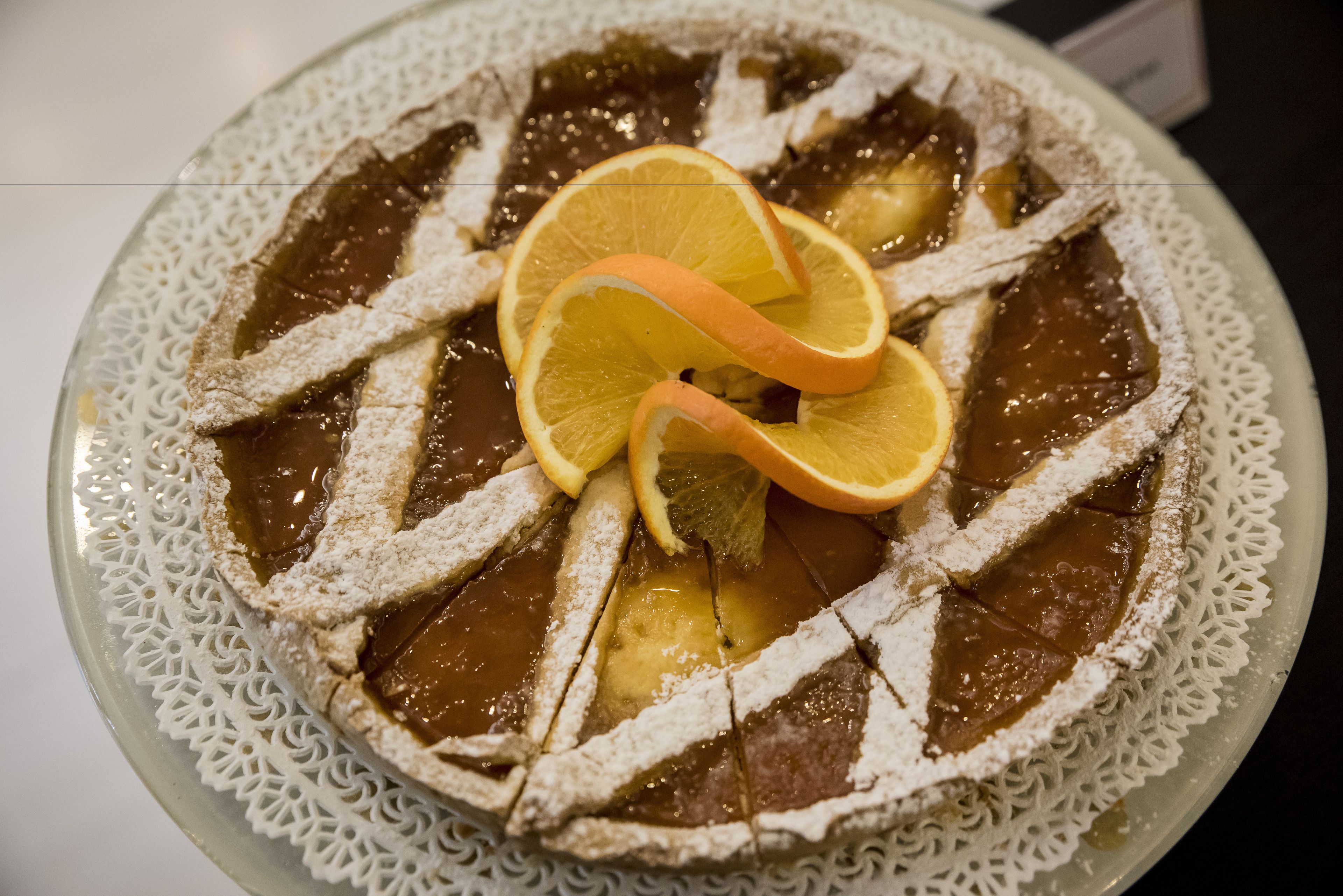 Un gâteau rond, surmonté d’une serviette de table en dentelle, saupoudré de sucre glace et décoré de tranches d’orange.