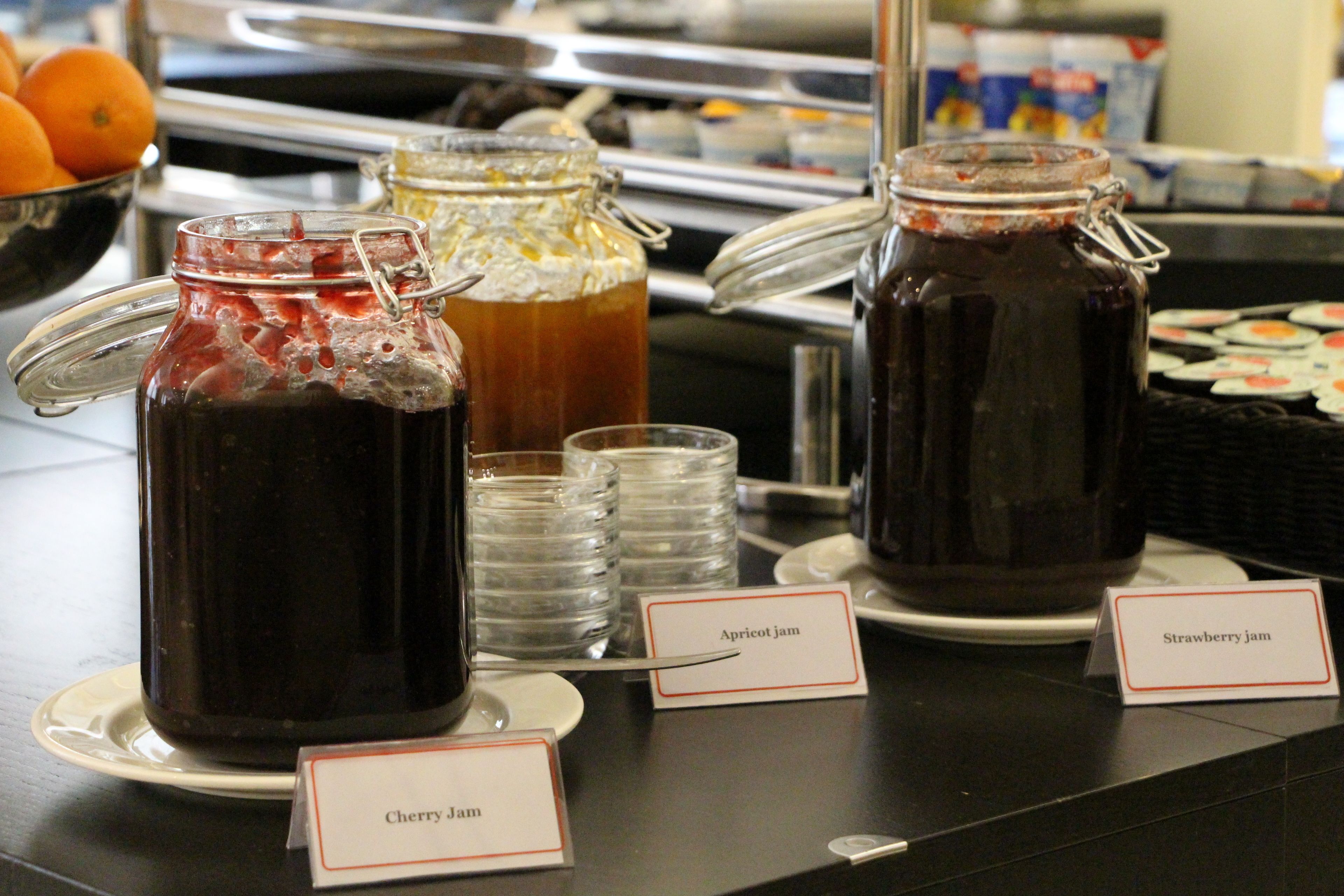 Un buffet con diversi vasetti di marmellata etichettati ciliegia, albicocca e fragola.