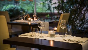 A dining table set with wine glasses, a candle, and cutlery, with a view of greenery outside. - Hotel Executive (Siena)