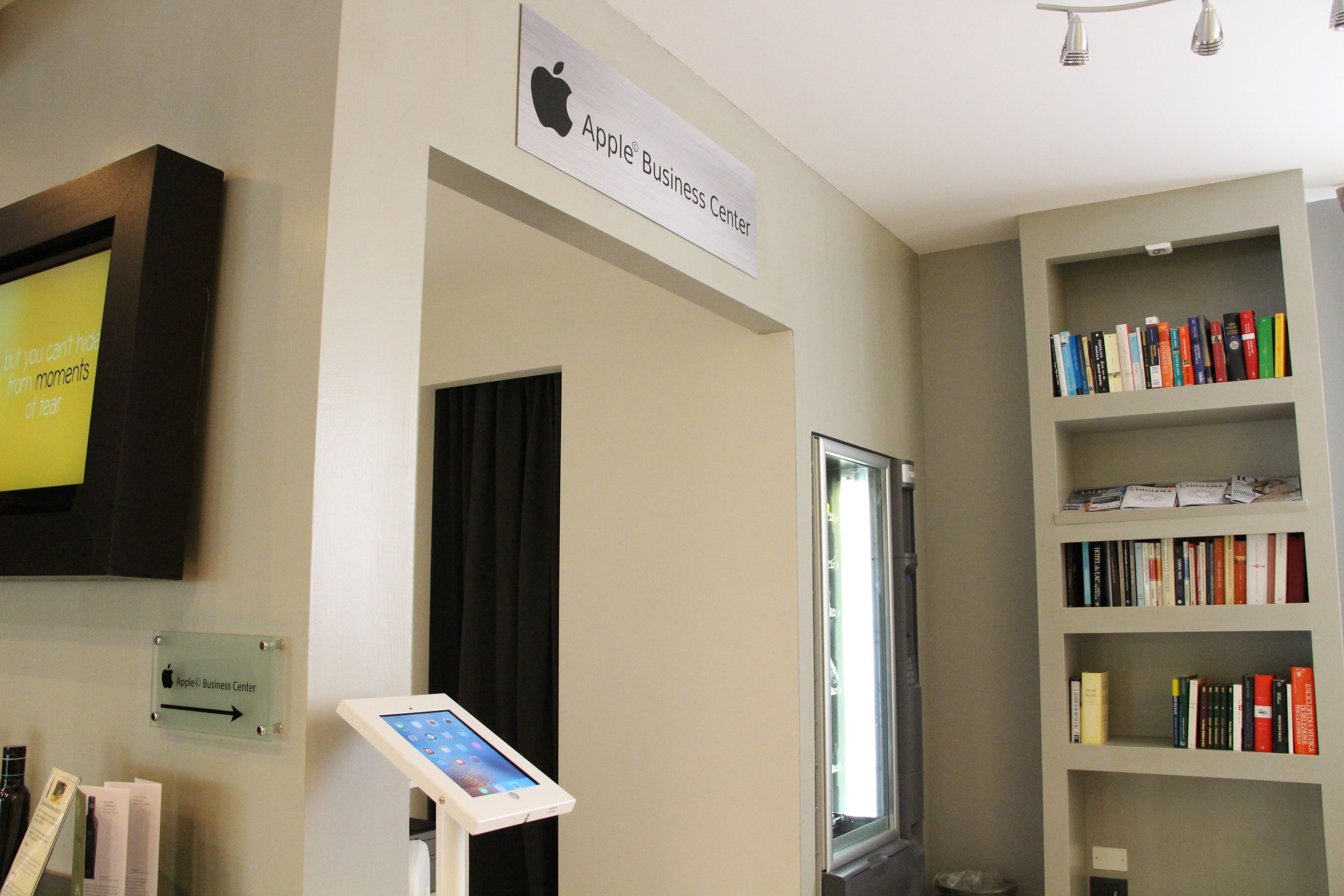 Une pièce avec une enseigne indiquant le «Centre d’affaires Apple», une fenêtre et une bibliothèque remplie de livres.