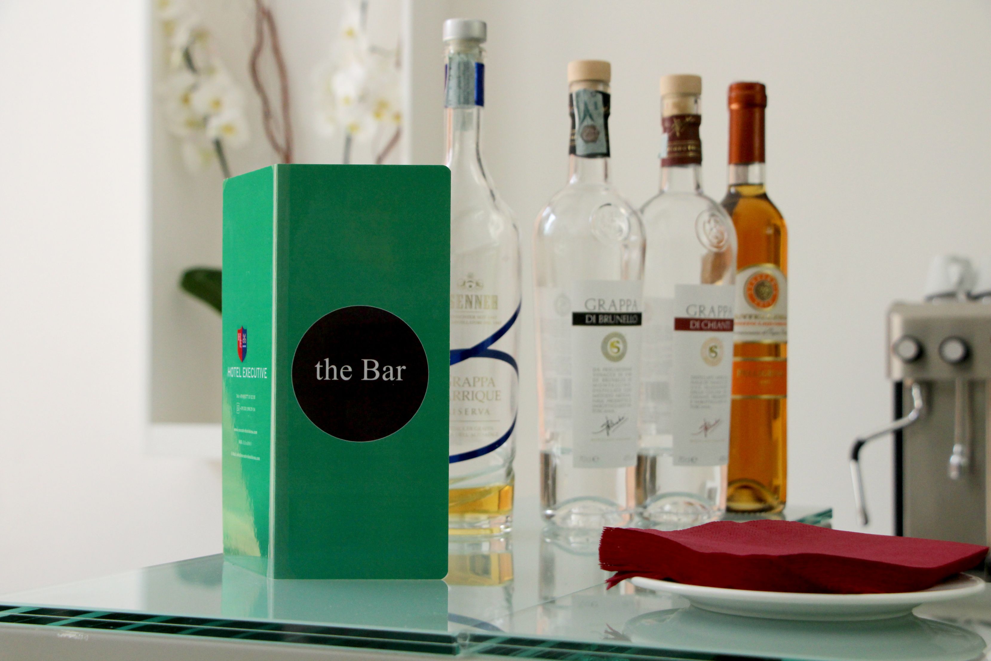 A bar area with a green sign labeled "the Bar" and several bottles of alcohol on a glass table.