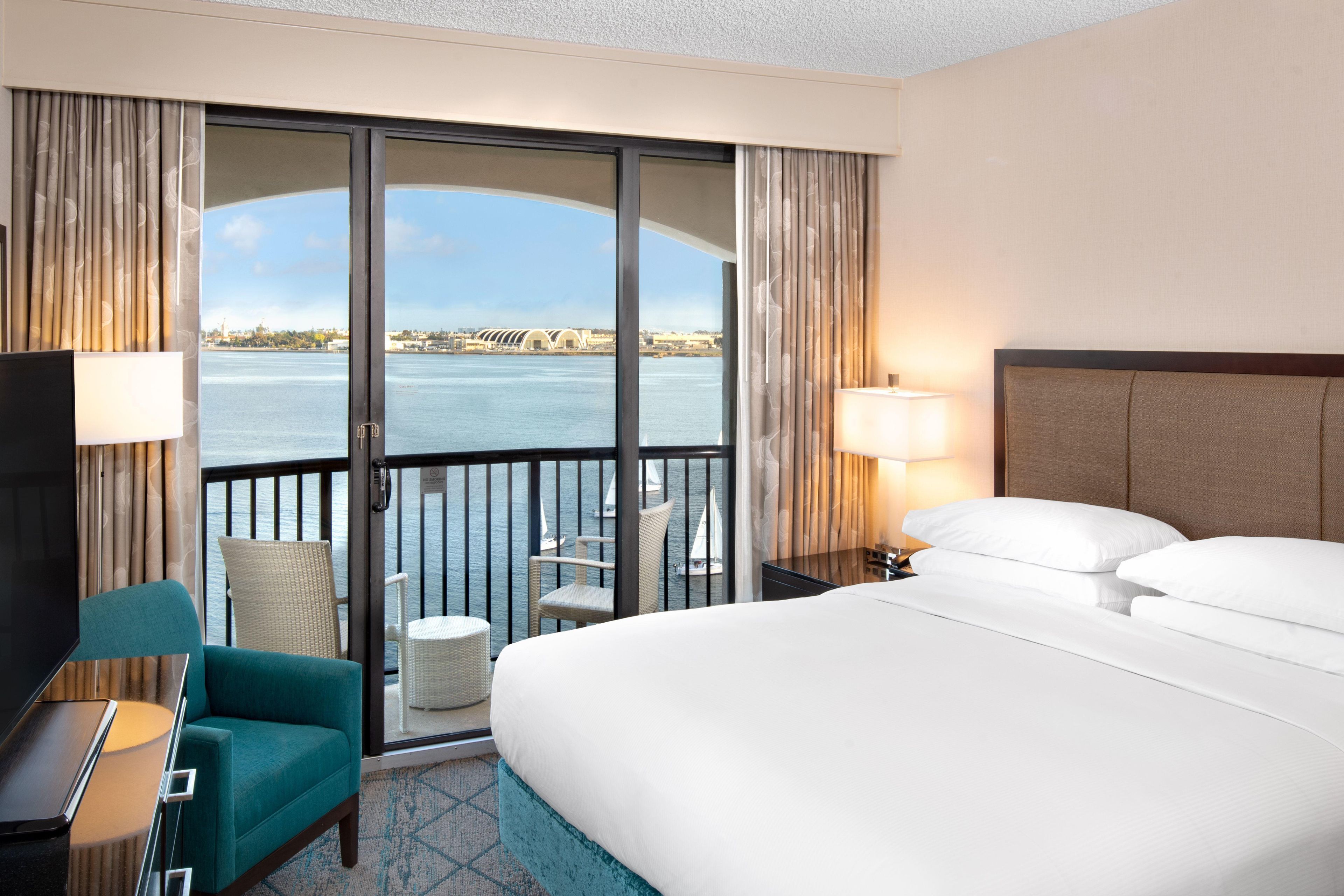 A hotel room with a large bed, a desk, a chair, and a view of the water.