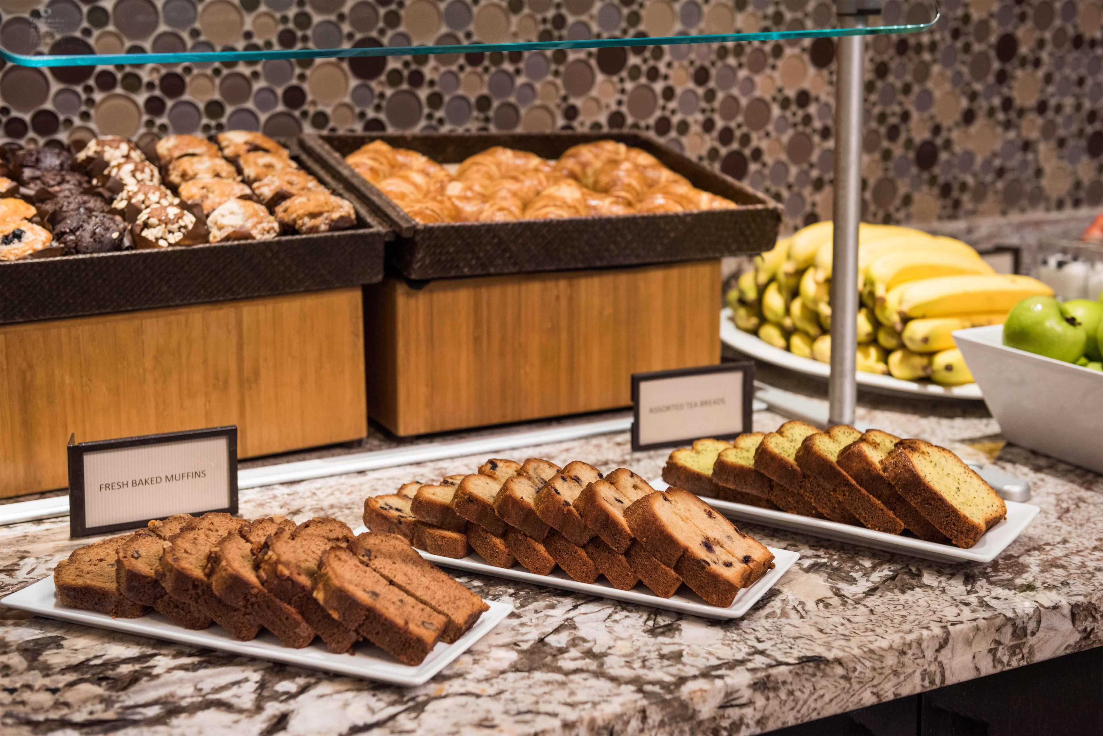 A buffet with various baked goods, including muffins and bread, displayed on a marble countertop.