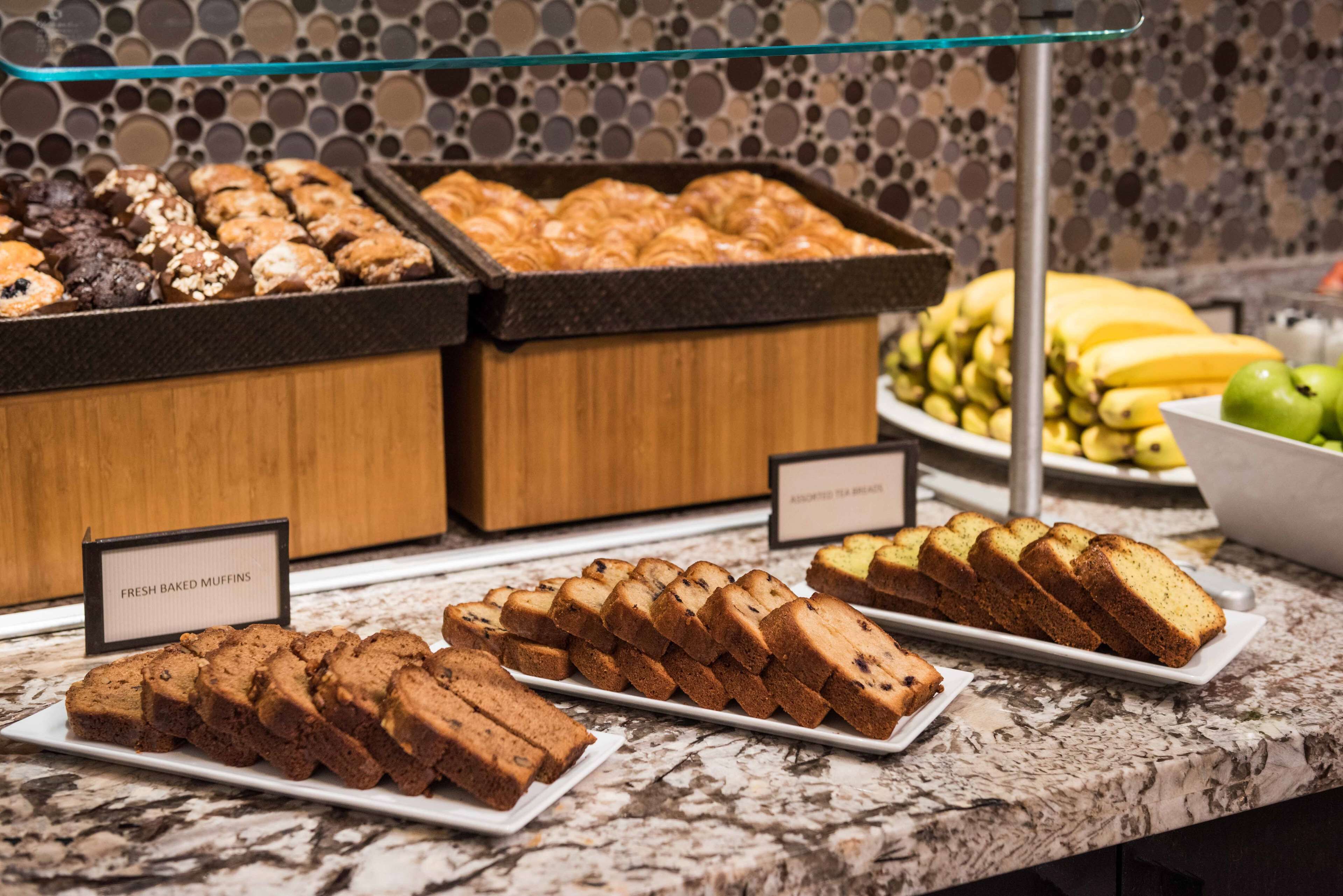 A buffet with fresh baked muffins, assorted tea breads, and a variety of fruits including bananas and apples.