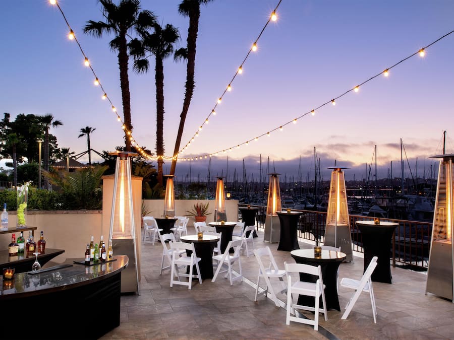 An outdoor patio with string lights, tables, chairs, and a bar area with bottles.