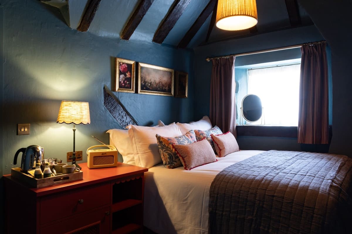 Une chambre à coucher avec un lit, une table de chevet, une lampe et une fenêtre avec des rideaux.