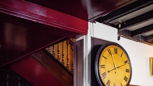 A grand staircase with wooden railings, a large wall-mounted clock, and a leather sofa in a warmly lit room with patterned flooring. - The White Hart - A Heartwood Inn (Lewes)