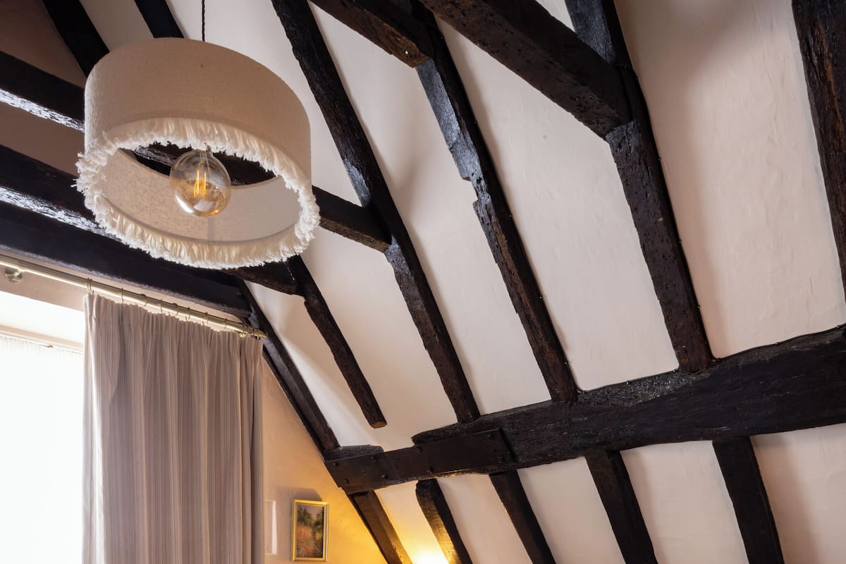 Une chambre avec un grand lit, un luminaire suspendu et des poutres apparentes.