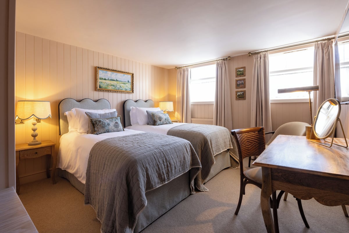 Une chambre d’hôtel avec deux lits, un bureau avec un miroir et une chaise.
