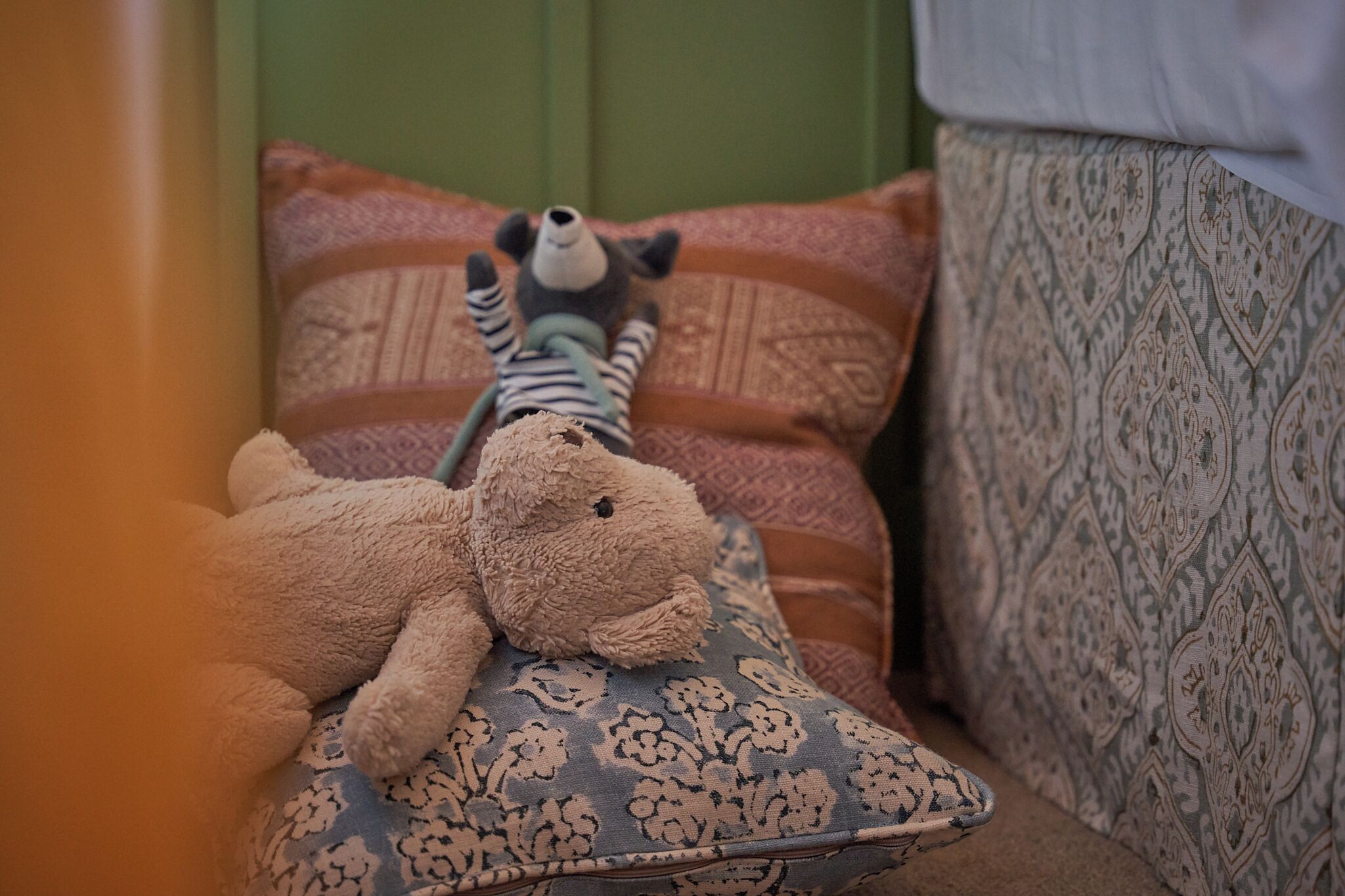 Un peluche sobre un cojín estampado en una habitación con cabecera verde y tapicería decorada.