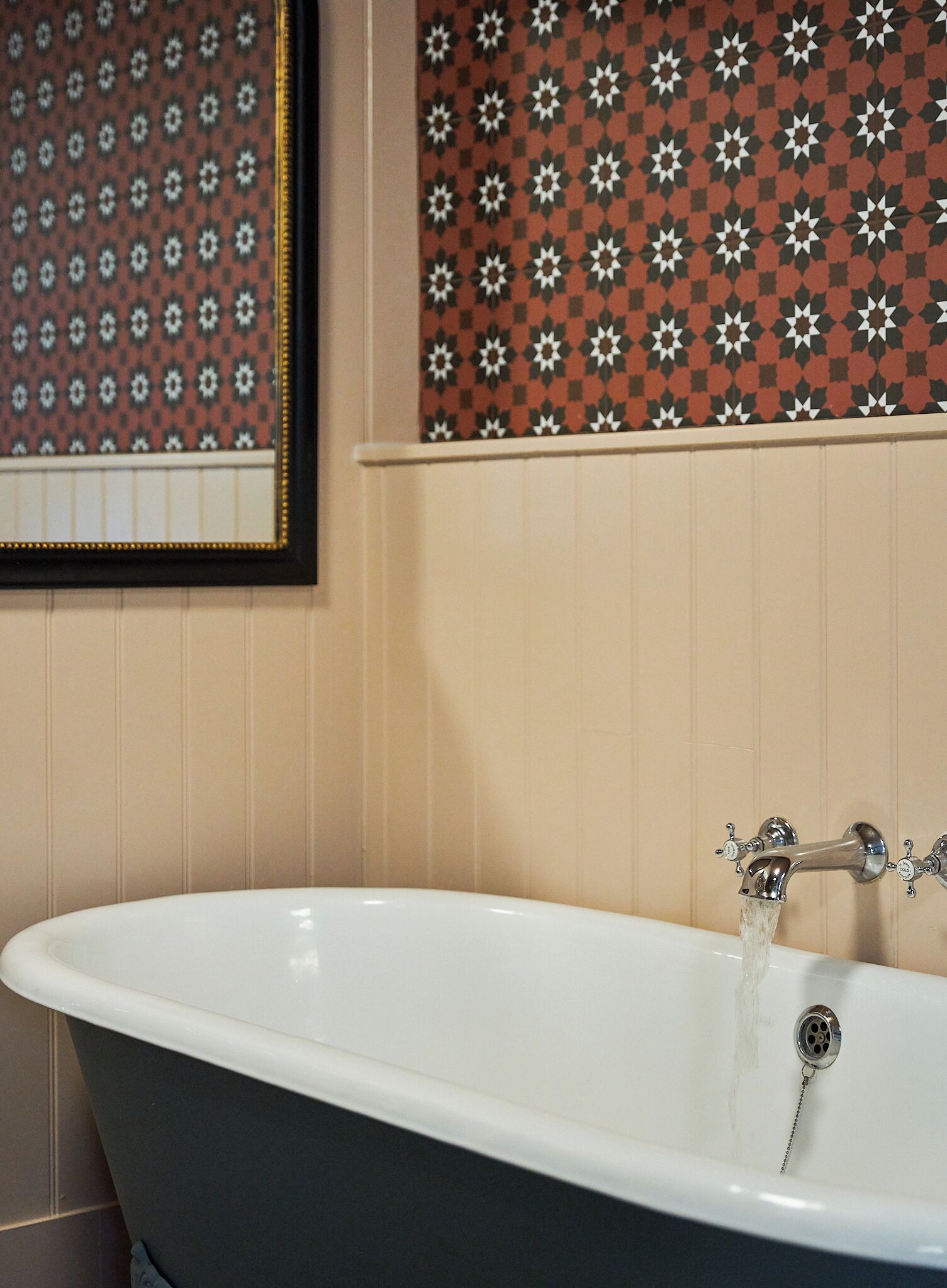 A bathroom with a freestanding bathtub, a wall-mounted sink, and patterned wallpaper.