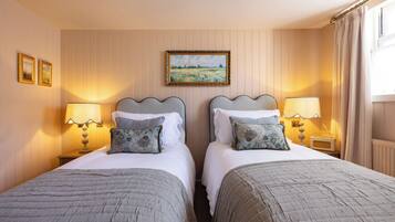 A hotel room with two beds, each with a headboard, bedside lamps, and decorative pillows. There is a framed painting on the wall above the beds.