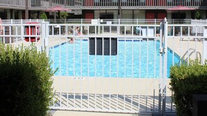 A pool area with a white fence, a red lifeguard chair, and a building with balconies in the background.