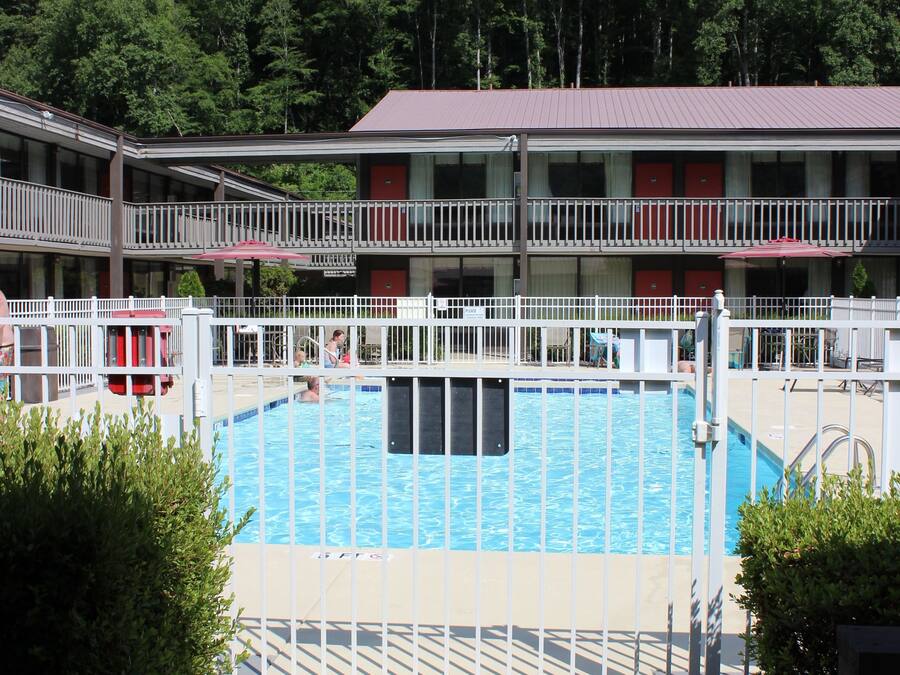Ein Poolbereich mit weißem Zaun, einem roten Rettungsschwimmerstuhl und einem Gebäude mit Balkonen im Hintergrund.