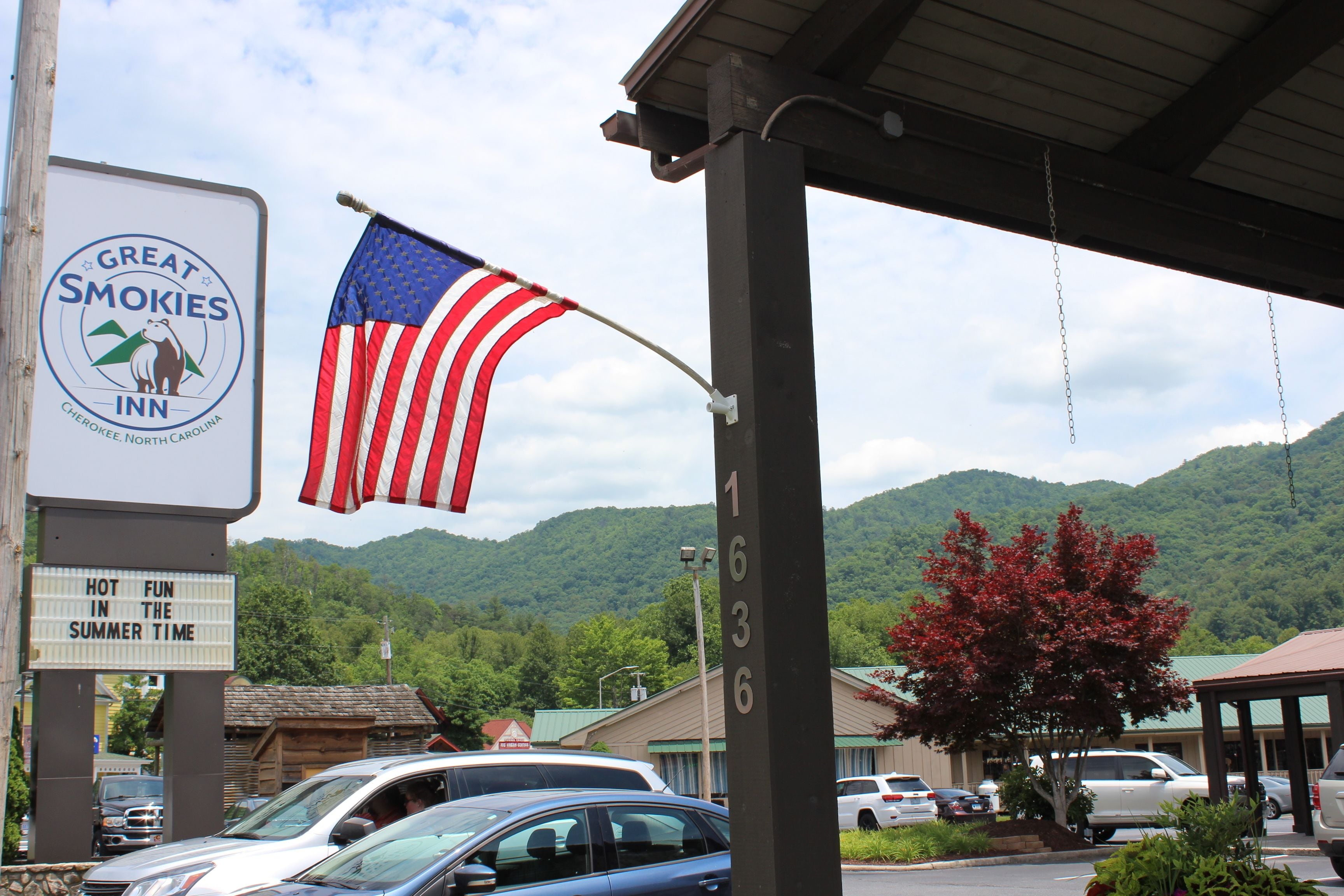 A motel sign with a mountain backdrop, a flag, and parked cars.