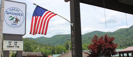 A motel sign with a mountain backdrop, a flag, and parked cars.