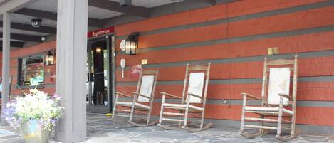 A building entrance with a registration sign, a lobby sign, and three rocking chairs lined up against a wall.