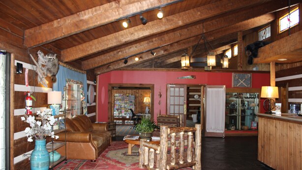 A spacious lobby with a wooden ceiling, a brown leather sofa, a coffee table, and a wooden chair. There is a vase with flowers on a table, and a red rug on the floor. - Great Smokies Inn Cherokee (Cherokee)