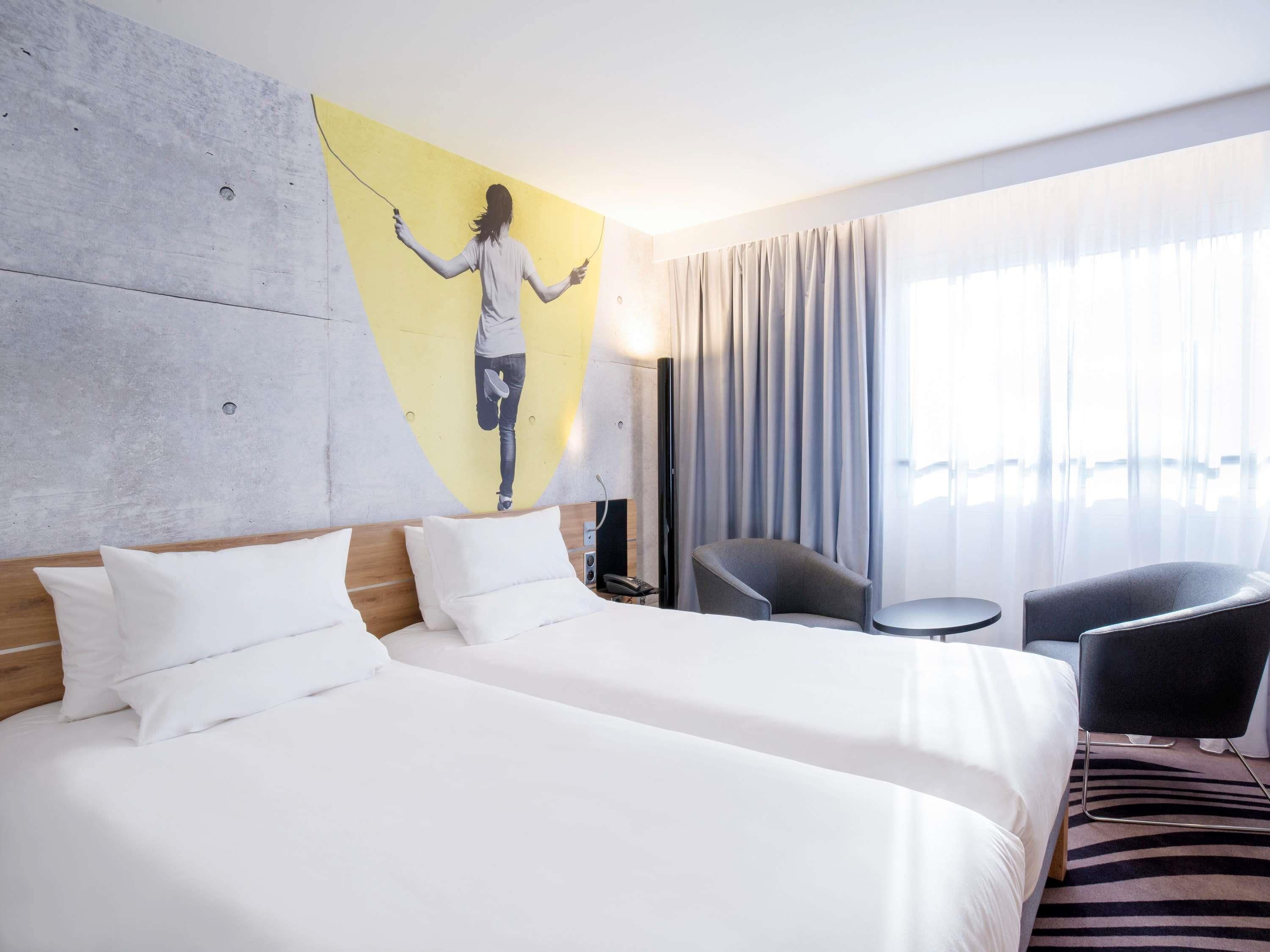 A hotel room with a large bed, a chair, a small table, and a painting on the wall.