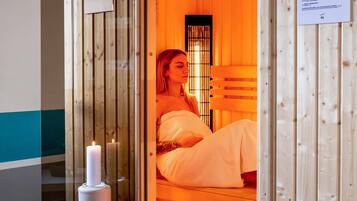 A sauna room with a wooden interior, a candle, and a person sitting on a bench.