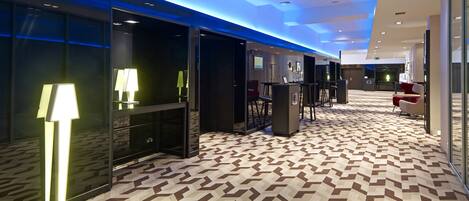 Un corridoio di un hotel con tappeto decorato, illuminazione moderna e porte vetrate che conducono alle camere.
