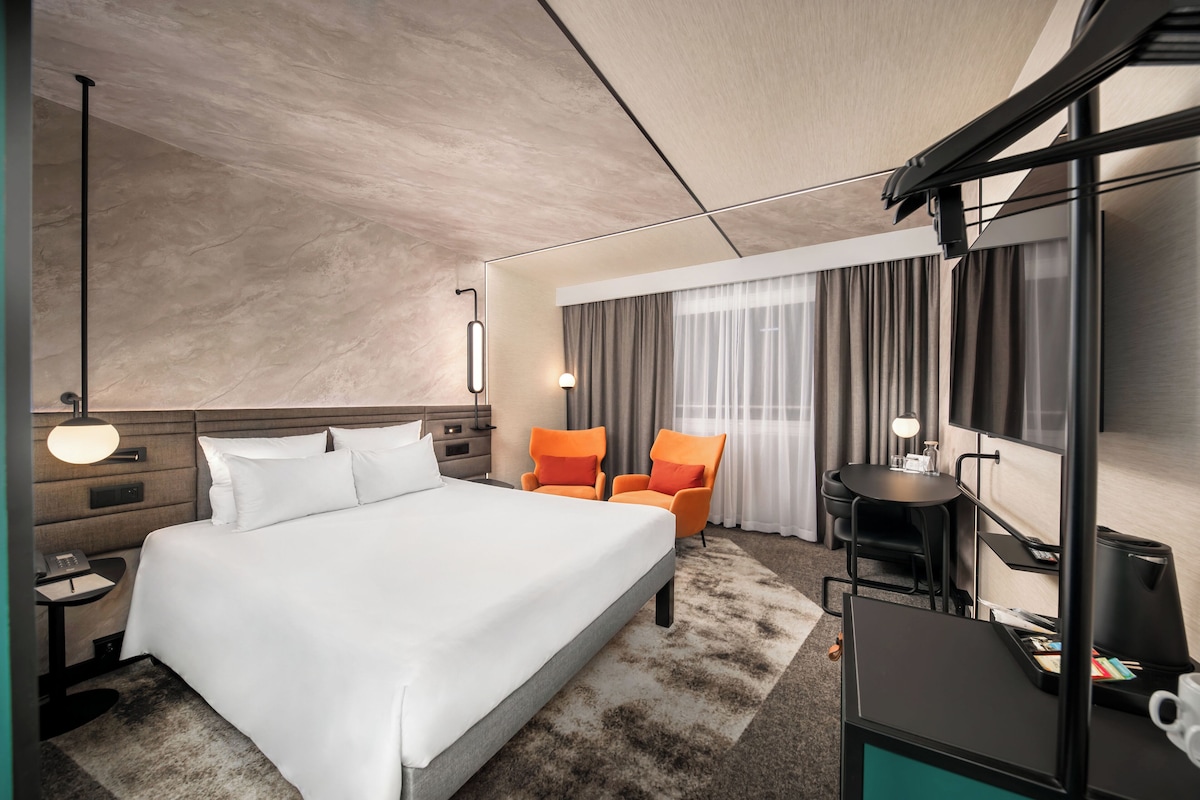 A hotel room with a bed, a desk, a chair, a TV, and a window with curtains.