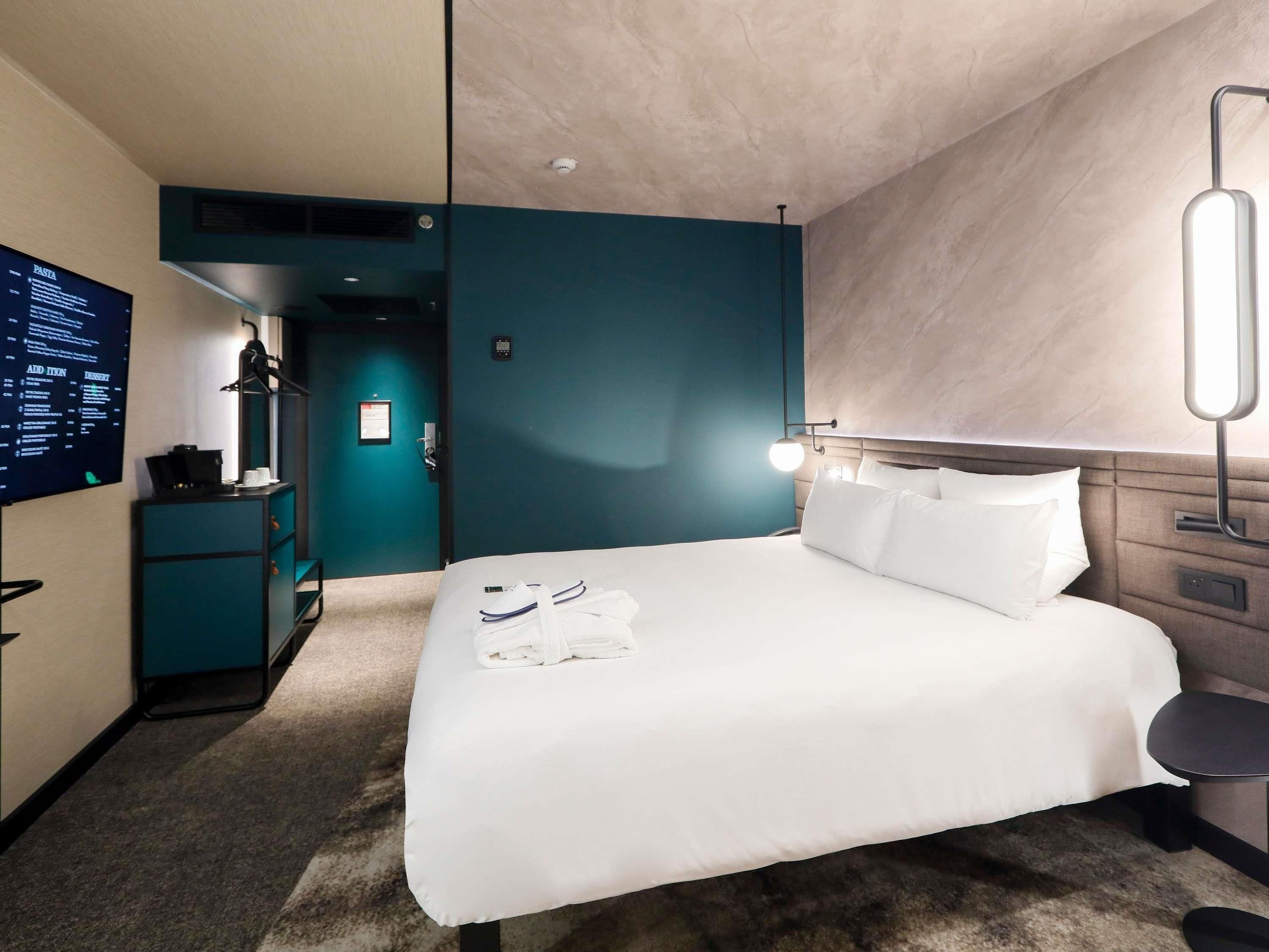 Une chambre d’hôtel équipée d’un lit, d’un bureau avec un ordinateur, d’une télévision et d’une lampe fixée au mur.