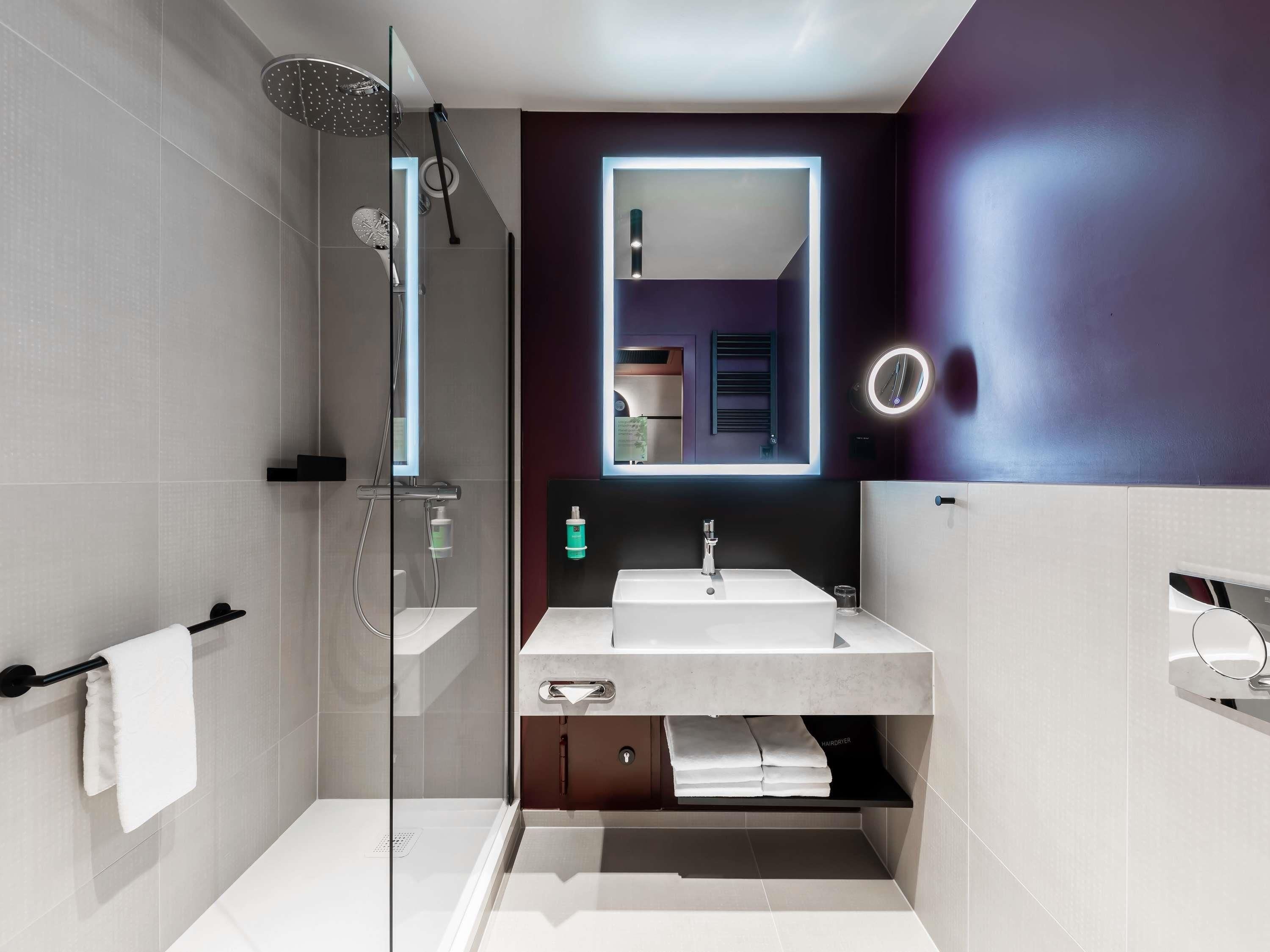 A modern bathroom with a glass-enclosed shower, a vanity with a mirror, and a towel rack.