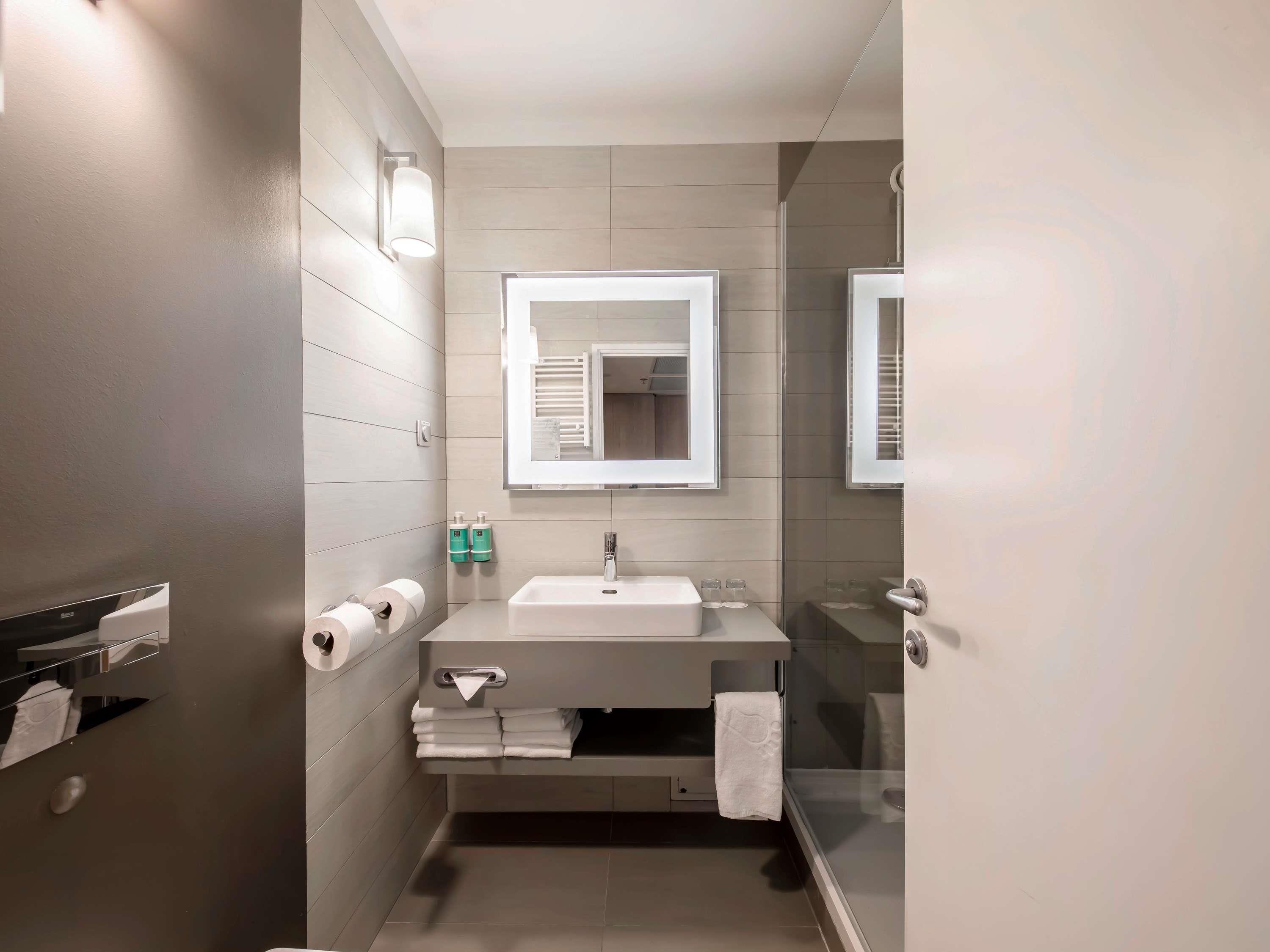 A modern bathroom with a sink, mirror, towel rack, and toilet paper.