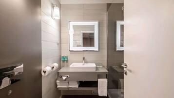 A modern bathroom with a sink, mirror, towel rack, and toilet paper.