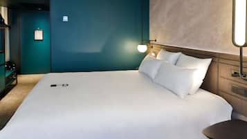 Una habitación de hotel moderna con una cama grande, una mesita de noche, una lámpara de pared y una puerta con un cartel.