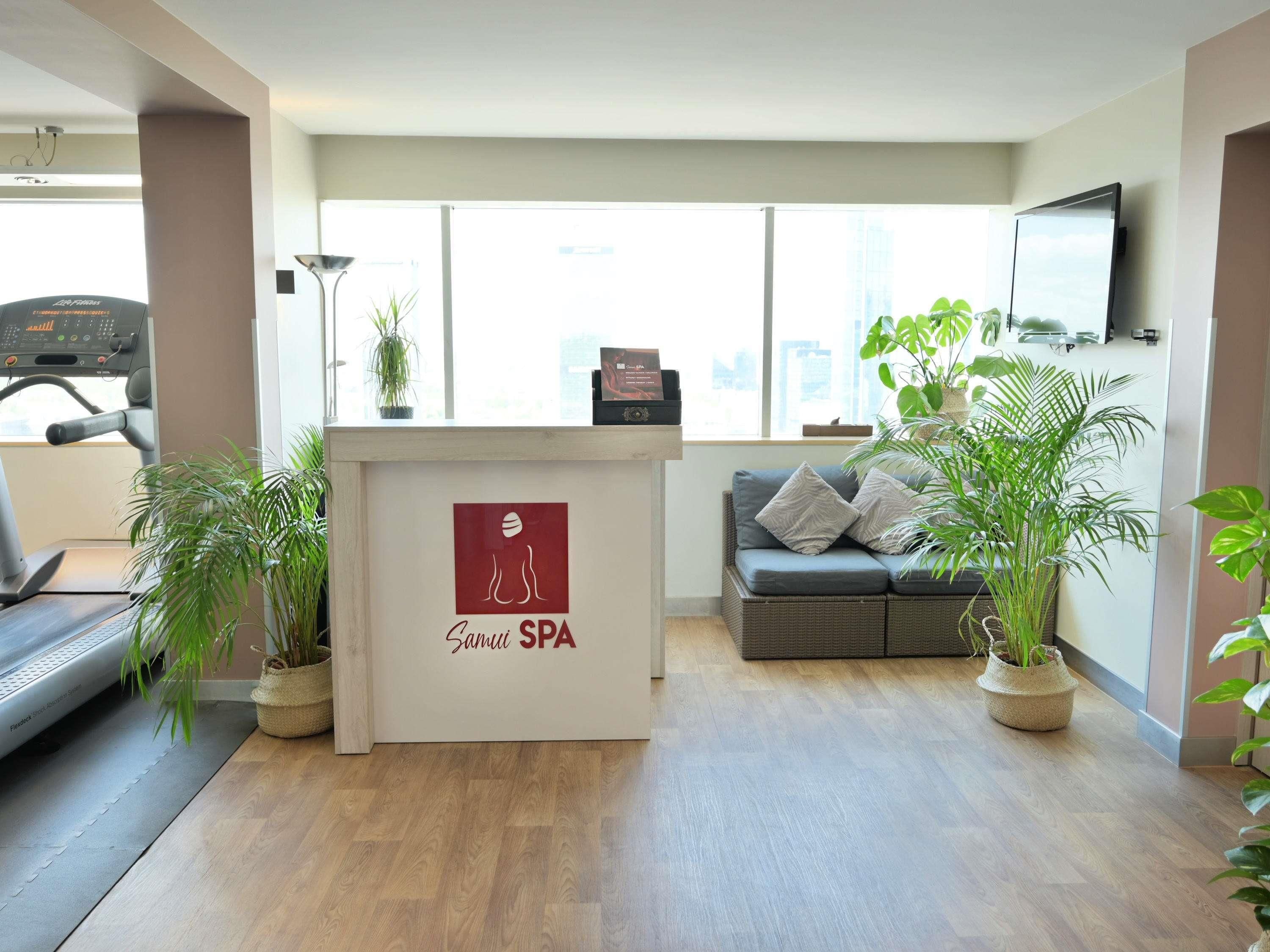 A reception area with a reception desk, a treadmill, a sofa, and potted plants.