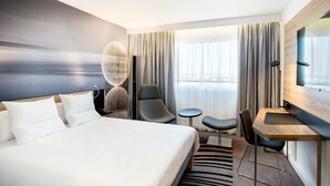 A modern hotel room with a large bed, a desk, a chair, and a small table.