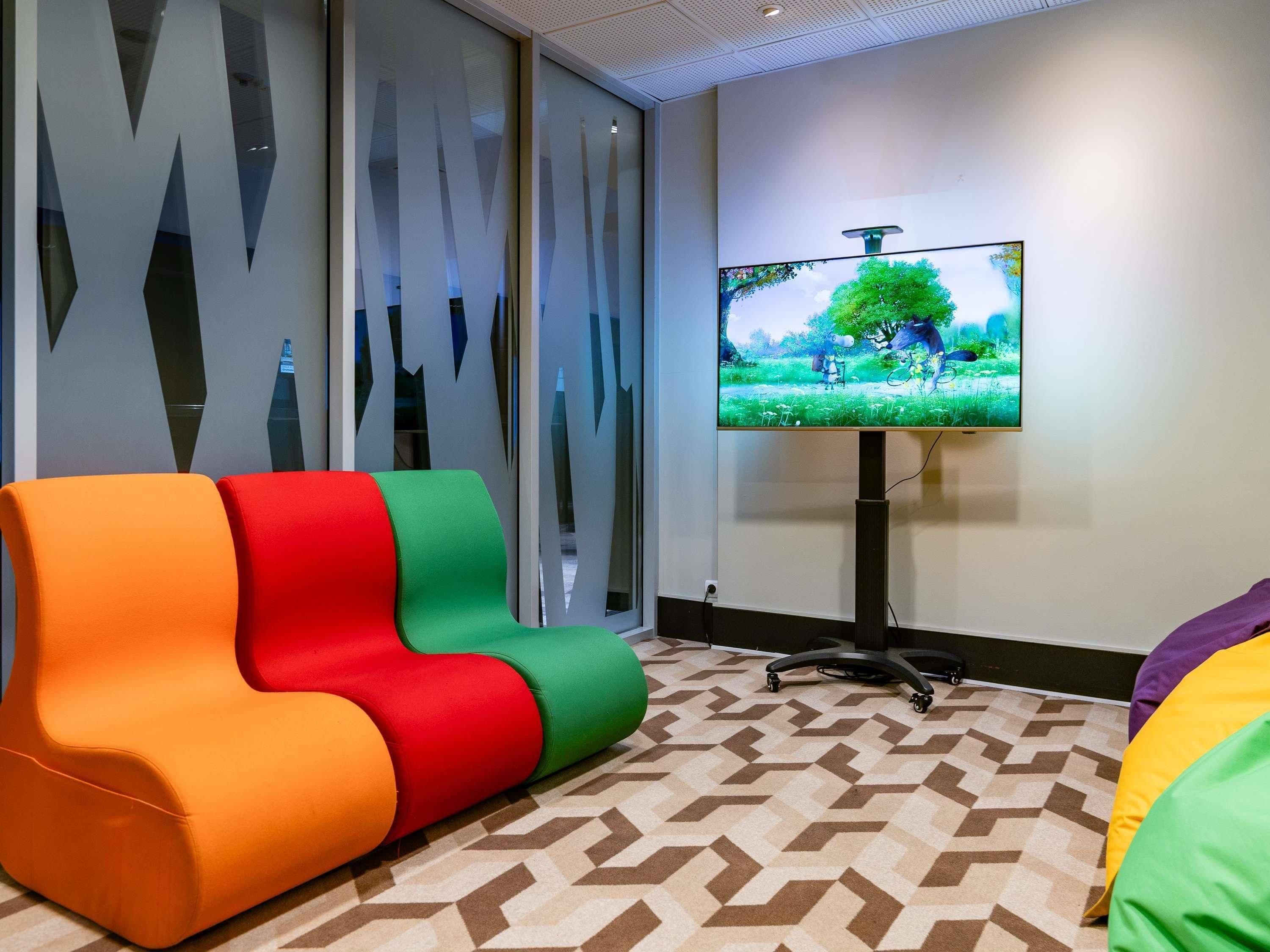 Una habitación moderna con un sofá colorido, un televisor sobre un mueble bajo y una alfombra estampada.
