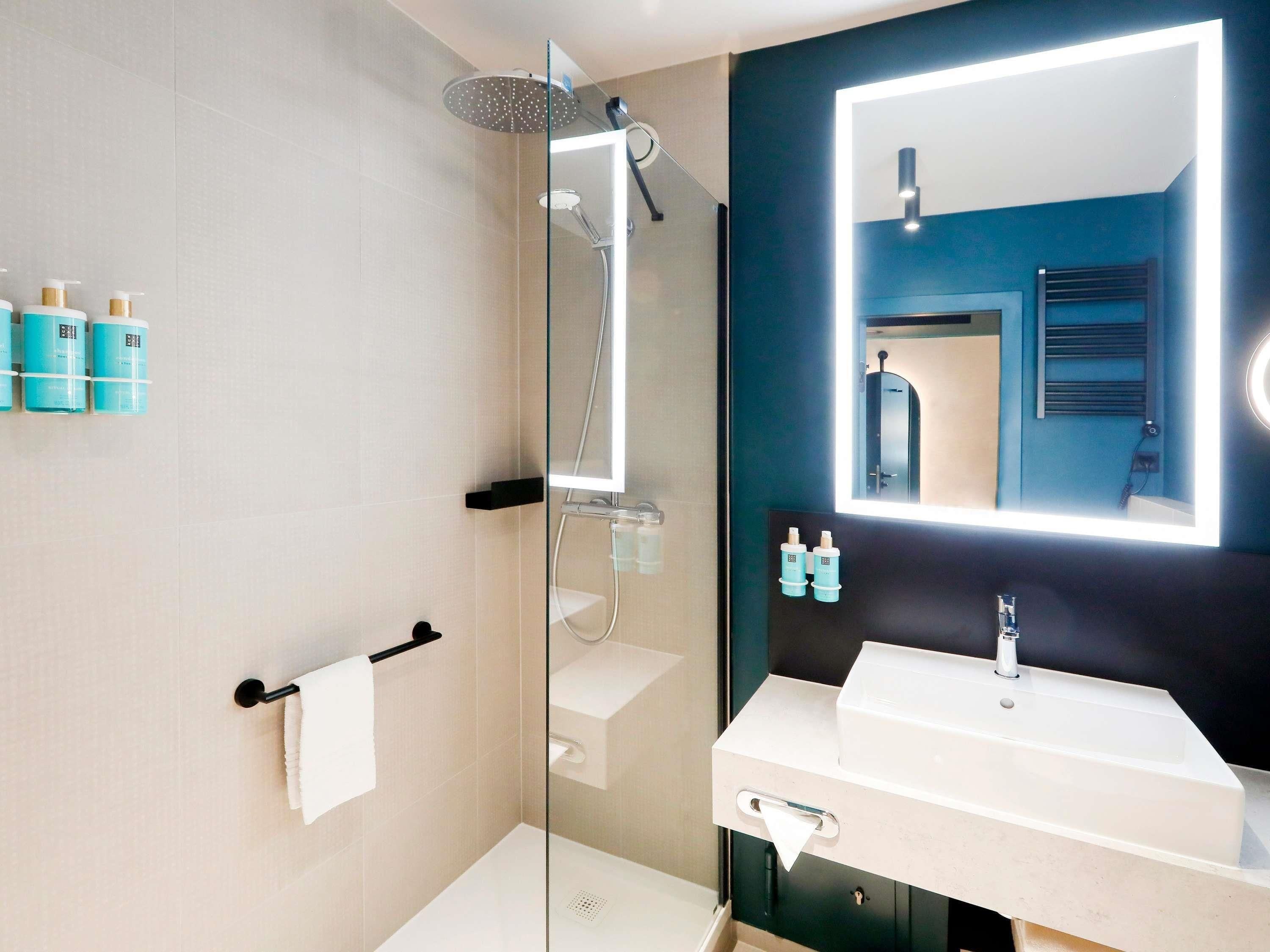 A modern bathroom with a glass shower enclosure, a large mirror, and a white sink.