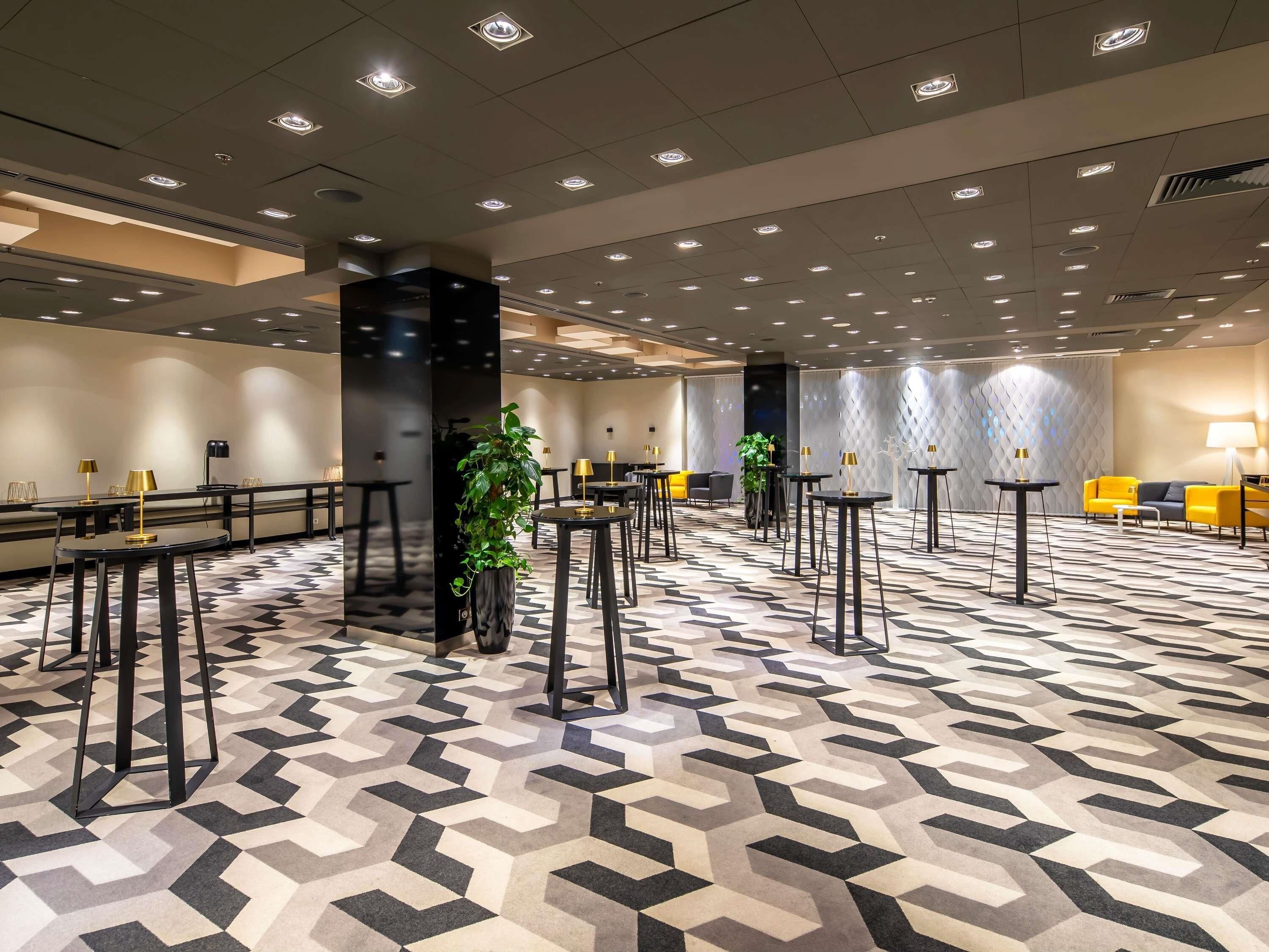 Eine geräumige Hotelhalle mit einem geometrischen Fußbodenmuster, mehreren Tischen mit Lampen und einem modernen Deckenstil.
