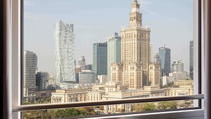 A view of a cityscape through a window, featuring a prominent historic building with a clock tower, surrounded by modern skyscrapers. - Novotel Warszawa Centrum (Warsaw)