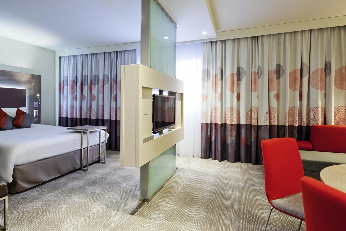 Ein Hotelzimmer mit Bett, Fernseher, Sitzecke und Vorhängen.