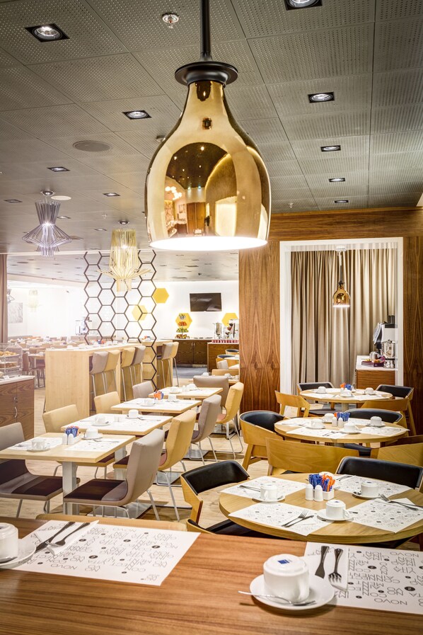 A modern dining area with round tables, wooden chairs, and a central hanging light fixture. - Novotel Warszawa Centrum (Warsaw)