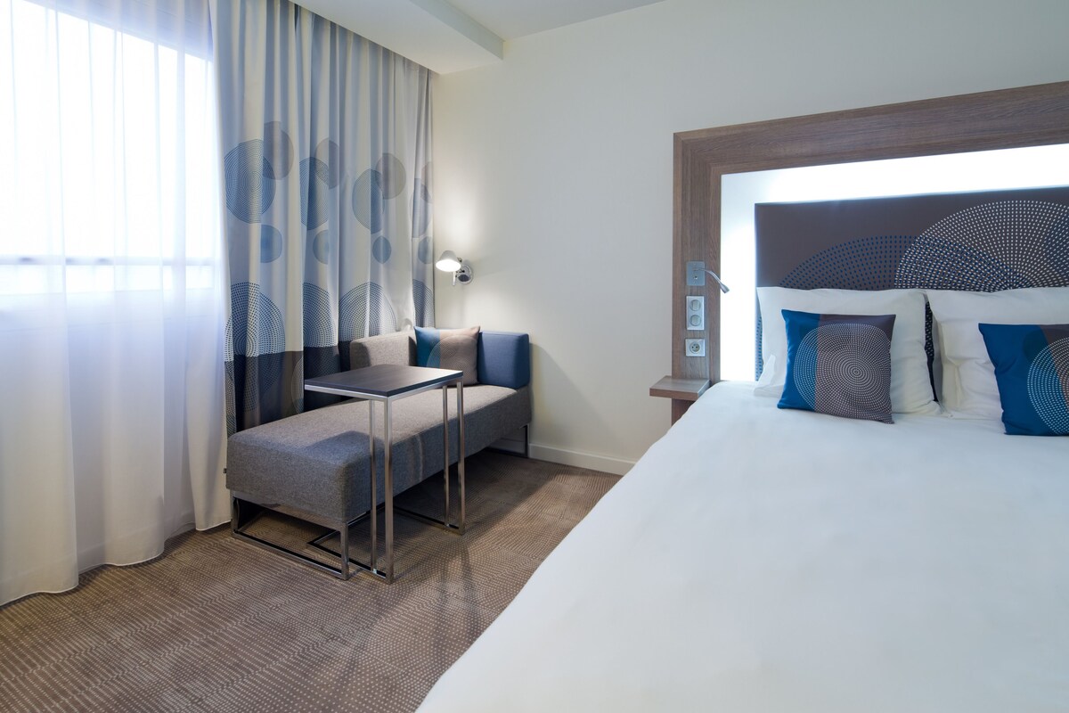 A hotel room with a large bed, a small table, a sofa, and a desk.