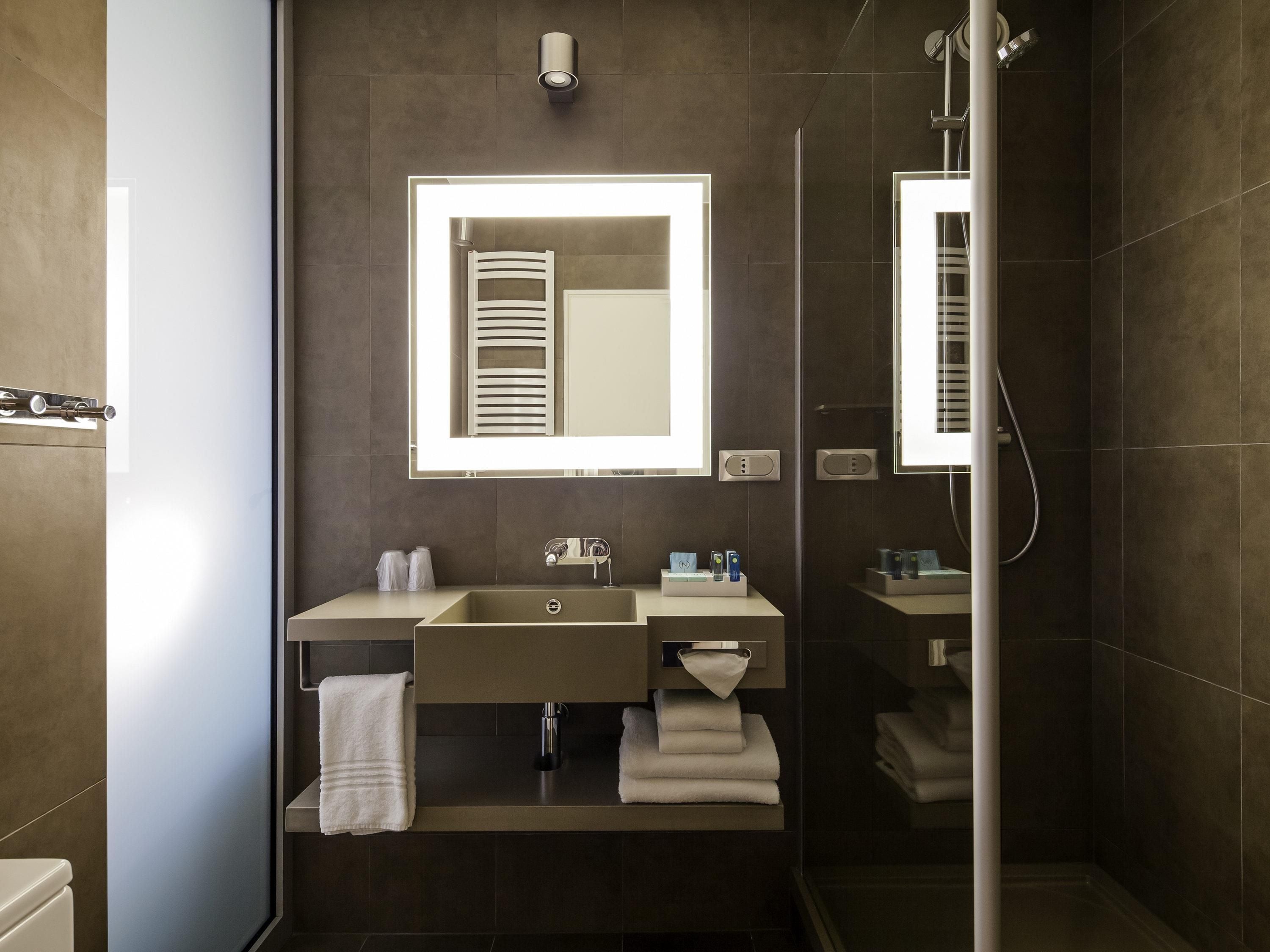 A modern bathroom with a large mirror, a sink, a towel rack, and a shower.