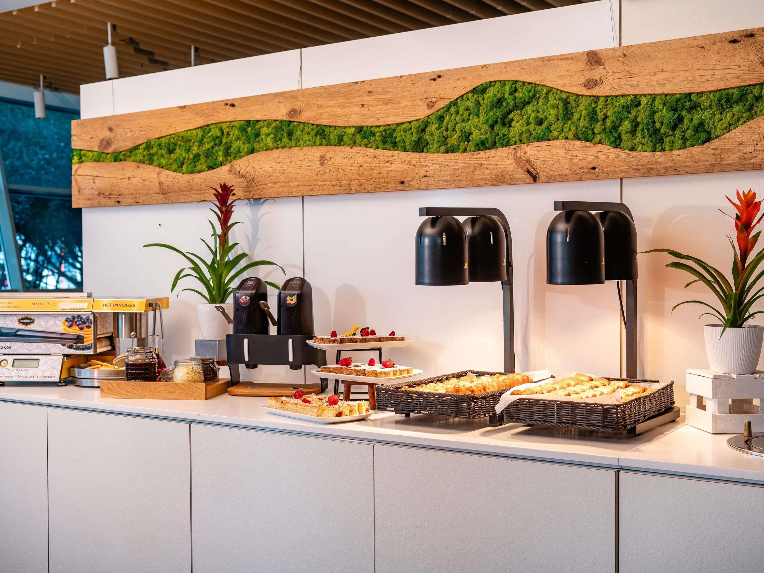A buffet counter with various food items, a coffee machine, and a wall-mounted green moss decoration.