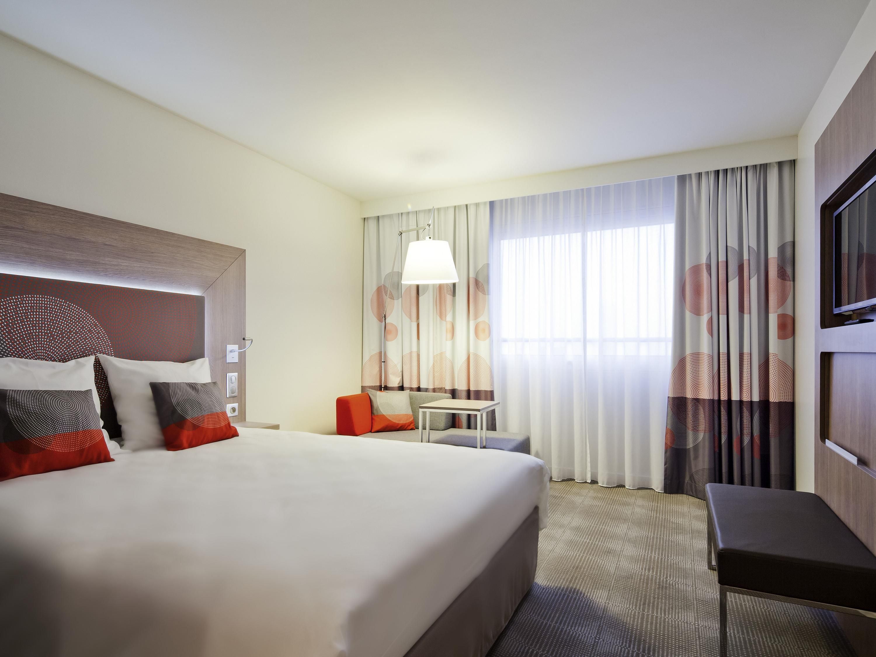 A hotel room with a large bed, a desk, and a TV on the wall.