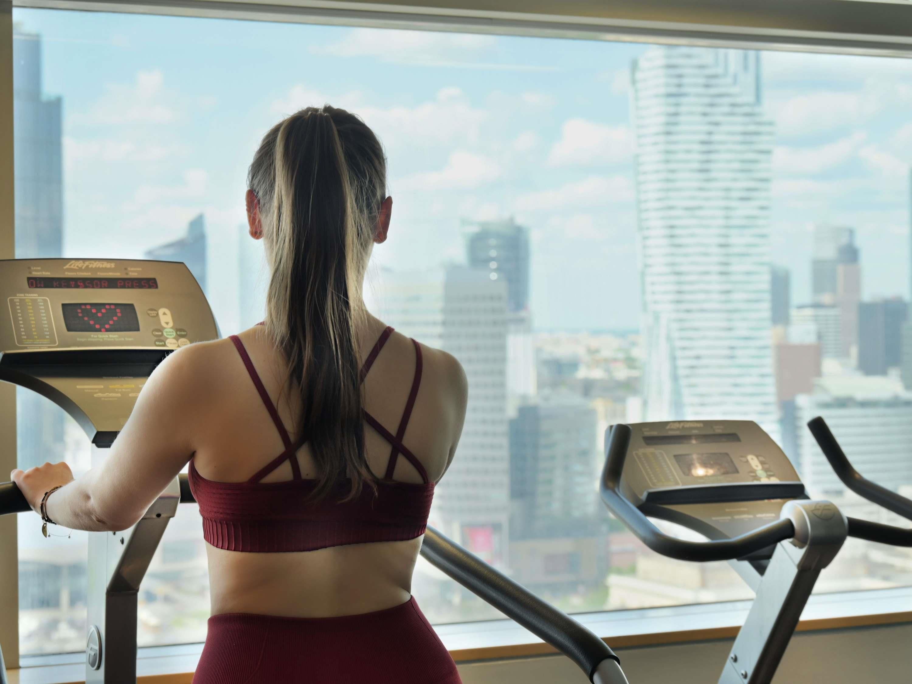 A person using a treadmill in a room with a large window overlooking a cityscape.